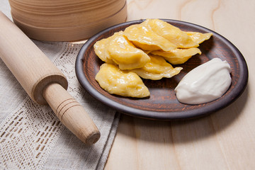 Fresh boiled varenyky or dumpling with cottage cheese or curd on clay plate and with sour cream on wooden background..