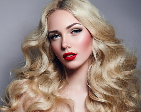 Beautiful young girl with luxurious light wavy hair close-up in the studio. Blonde - shiny, light long hair, curls. Makeup - arrows, red lipstick, pink blush. Cosmetics, hair care.