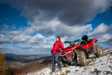Atv quad bike near guy in winter clothes looking into the distance on snowy mountain slope. On the...