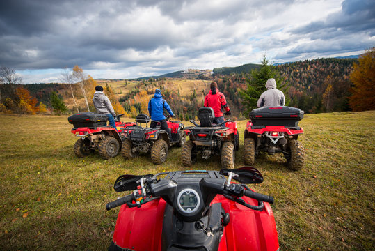 View from quad bike. Four men at ATV enjoying beautiful landscape of rolling countryside and colorful forest under the sky with cumulus clouds in autumn