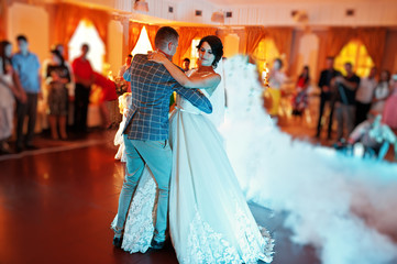 Beautiful wedding couple dancing their first dance in a restaurant with people in the background.