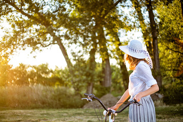 Beautiful young caucasian woman with a bicycle in park at summer sunny day