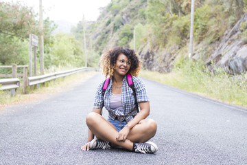 smiling girl sitting on the road with the backpack