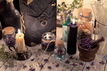Close up of magic book, dry flowers, glass jars and burning candles on the table. Mystic and occult still life, vintage background