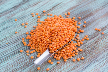 Batch of orange lentils scattered on spoon on wooden background