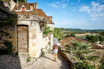 Young woman tourist with backpack and hat walking on the narrow street in the famous La Roque...
