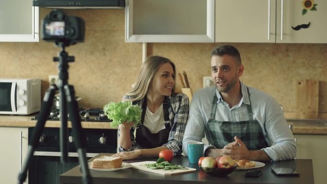 Young attractive couple shooting video food blog about cooking on dslr camera in the kitchen