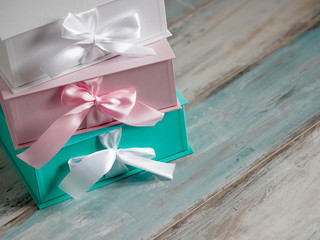 Three gift boxes, white, pink and turquoise. Wooden background.