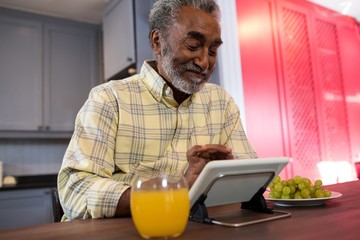 Fototapeta na wymiar Happy senior man using tablet computer in kitchen