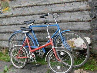 Fototapeta na wymiar Two old bicycles of blue and red colors on the background of a wooden house