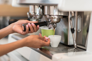Cropped shot of female barista using coffee machine while making coffee in cafe