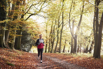 Mature Woman Running Through Autumn Woodland