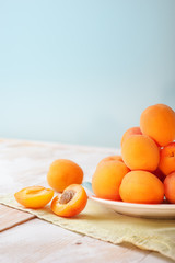 Vertical photo of Delicious ripe orange apricots in a bright plate on wooden table with green napkin on light blue wall background. Fresh juicy fruits. Bio vegetarian food village concept.