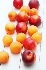 top view of white wooden background with juicy orange apricots and bright fresh red nectarines and peaches. Colorful composition of healthy fruits. Food vegetarian nutrition concept.
