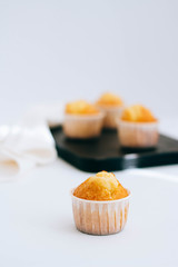 Orange muffins in the foreground and on a black tray