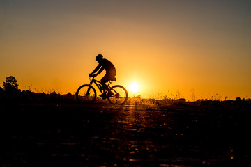 Fototapeta na wymiar Silhouette of cyclist riding on a bike on road at sunset.
