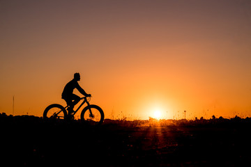 Fototapeta premium Silhouette of cyclist riding on a bike on road at sunset.