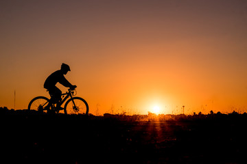 Fototapeta na wymiar Silhouette of cyclist riding on a bike on road at sunset.