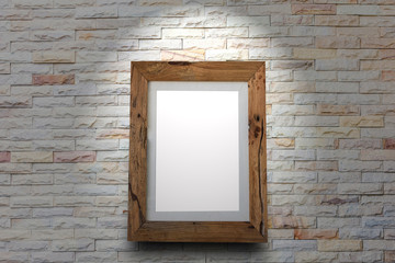 Empty wooden picture frame on a brick wall with spotlight.