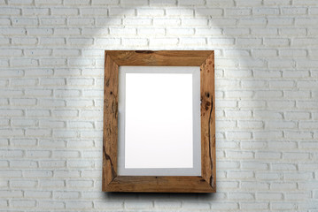 Empty wooden picture frame on a brick wall with spotlight.