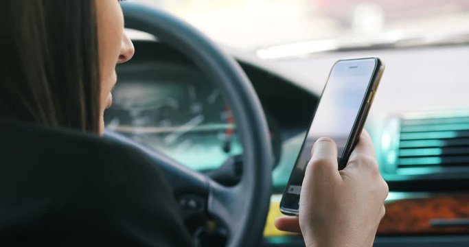 Beautiful woman is sitting in a car. holding a mobile phone and messaging. scrolling social media network apps The lady is looking forward happily. She is smiling auto automobile close up