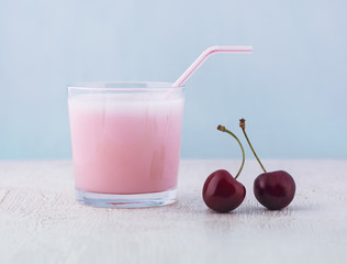 Glasses of a delicious milkshake and fresh cherries on a white wooden table