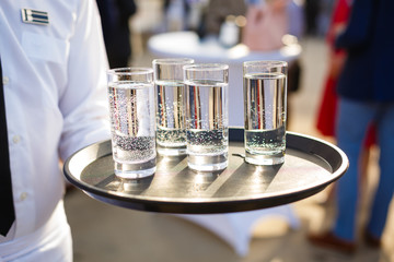Waiter carrying a tray with miniral water on an outdoors reception
