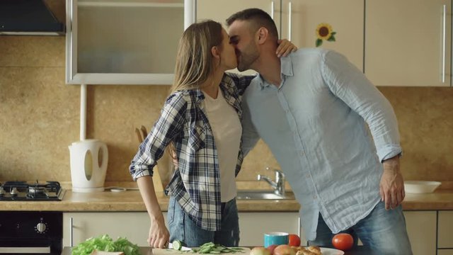 Happy young couple in the kitchen. Attractive woman cooking breakfast and cuff her boyfriend who want to taste food