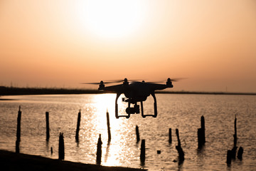 Fototapeta na wymiar Silhouette of drone over lake at sunset / Silhouette of drone over lake with destroyed wooden pier at sunset 