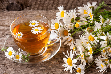 Herbal tea with fresh chamomile flowers on old wooden background