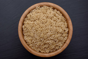 pasta in the form of asterisks lie in a wooden cup on a black stone board, space for text