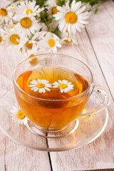 Herbal tea with fresh chamomile flowers on white wooden background