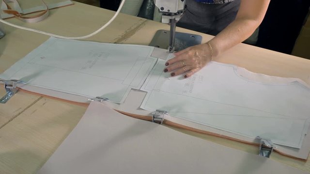 A tailor cuts clipped cloth with a vertical machine. 