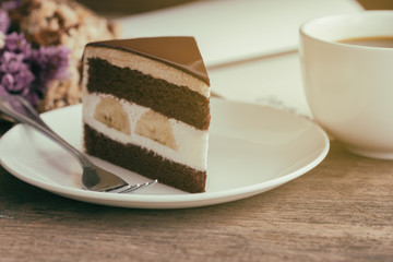 Banana chocolate cake on white plate served with black coffee. Chocolate cake layered with whipped cream and banana look so delicious. Enjoy eating at cafe restaurant with chocolate cake and coffee.
