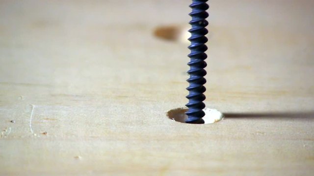 A sheetrock screw is tightened in countersunk hole in pine board with cordless drill and phillips head bit.  Macro shot from slight high angle looking down.  Audio included in clip