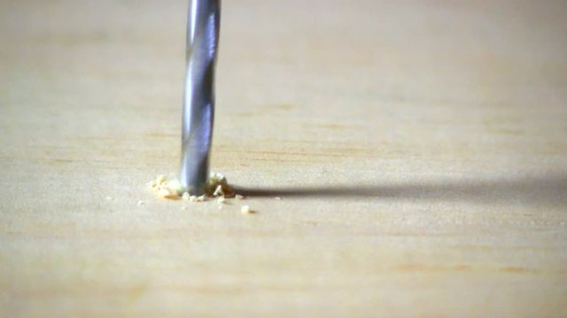 A hole is drilled into pine board with cordless drill & countersink bit.  Sawdust is then blown away.  Macro shot from slight high angle looking down.  Audio included in clip