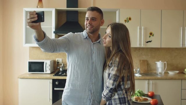 Young happy couple having online video chat in the kitchen at home