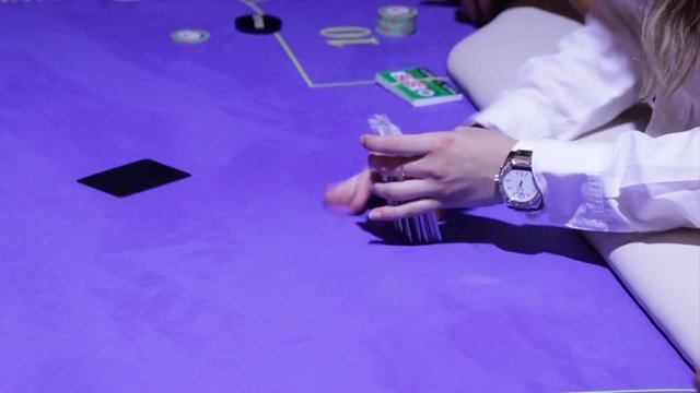 Croupier shuffling cards on poker table game in a casino.