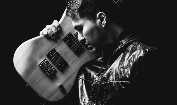 asian handsome rocker in black jacket posing on electric guitar, black and white. isolated on black