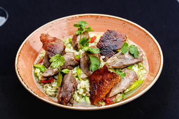 Baked duck served in a plate with rice and green beans and greens dressed with sauce.