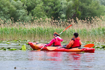 Couple man and woman - family kayaking in wild lake among thickets of plants on biosphere reserve in spring. Fun together enjoying adventurous experience with kayak during vacation