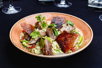Baked duck served in a plate with rice and green beans and greens dressed with sauce.