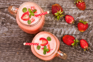 Glass of strawberry yogurt or smoothie with mint leaves on old wooden background. Top view
