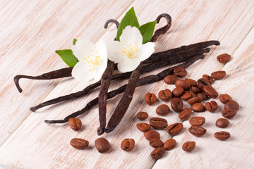 Vanilla sticks and coffee beans with flower and leaf on a white wooden background