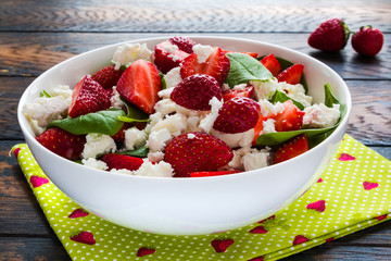 Salad with fresh strawberry, green spinach leaves and feta cheese in a white bowl on the wooden rustic table.