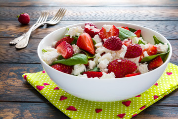 Healthy vegetarian salad with fresh strawberry, green spinach leaves and feta cheese in a white bowl on the wooden rustic table.