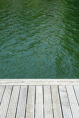 Grey teak wooden terrace with green water in the background.