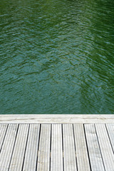 Fototapeta premium Grey teak wooden terrace with green water in the background.