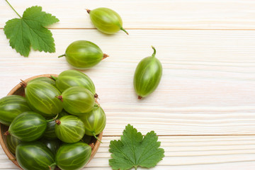 Gooseberry in wooden bowl on white wooden background.