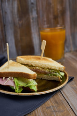 Club sandwich with cheese, ham, lettuce on plate and glass of Sea-buckthorn berries juice
